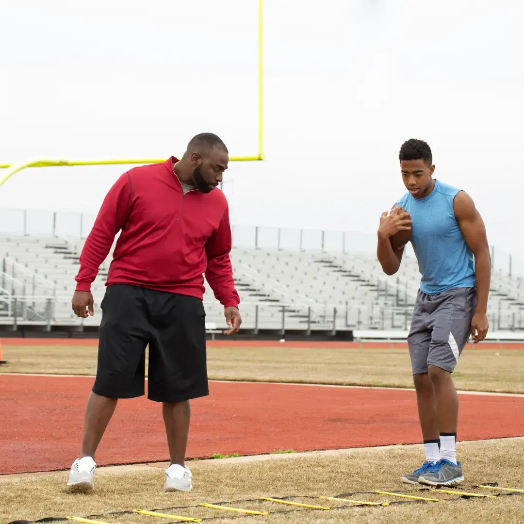 High school football coach training an athlete on field.
