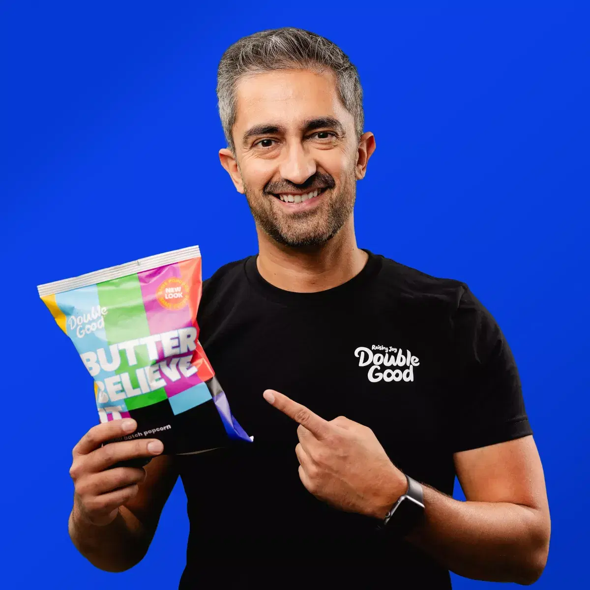 Anurag is holding a bag of popcorn in one hand, smiling and pointing with the other hand at the bag of popcorn.