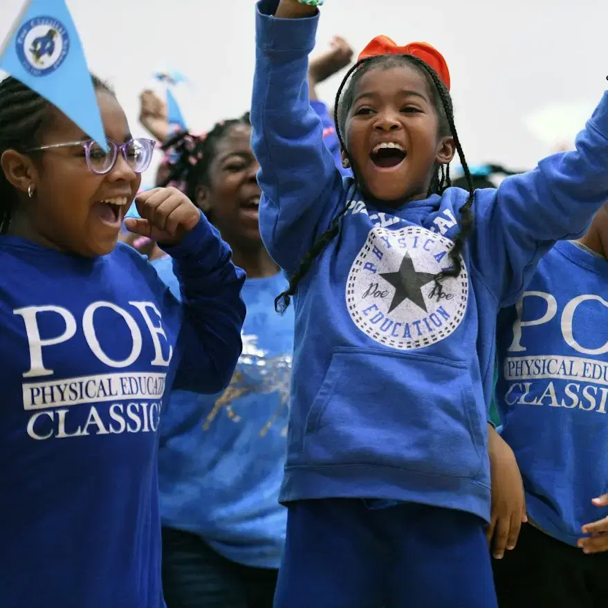 Children in blue shirts cheer enthusiastically, holding a small blue flag, with "POE Physical Education Classic" printed on their clothing.